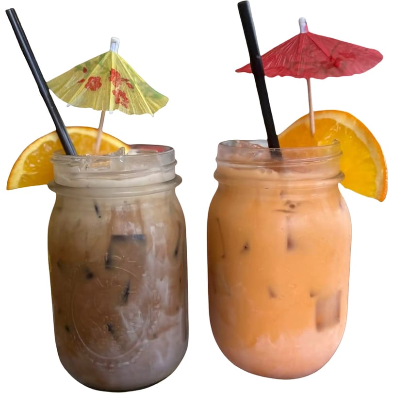 Two Thai iced drinks in mason jars, one coffee and one tea, garnished with orange slices and umbrellas.