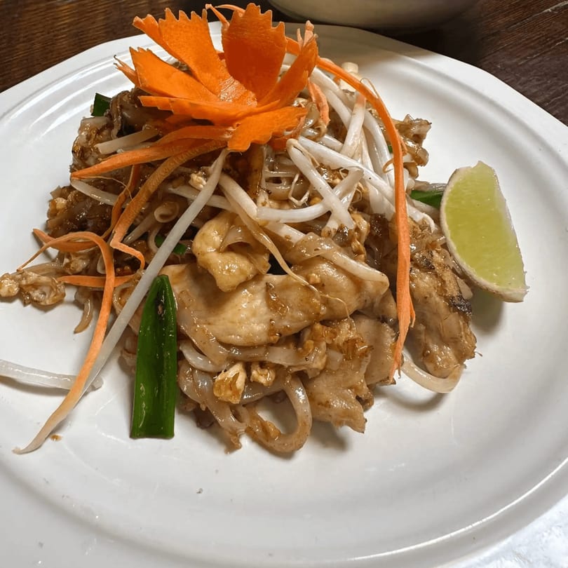 Chicken Pad See Ew with bean sprouts, carrot garnish, and a lime wedge on a white plate.