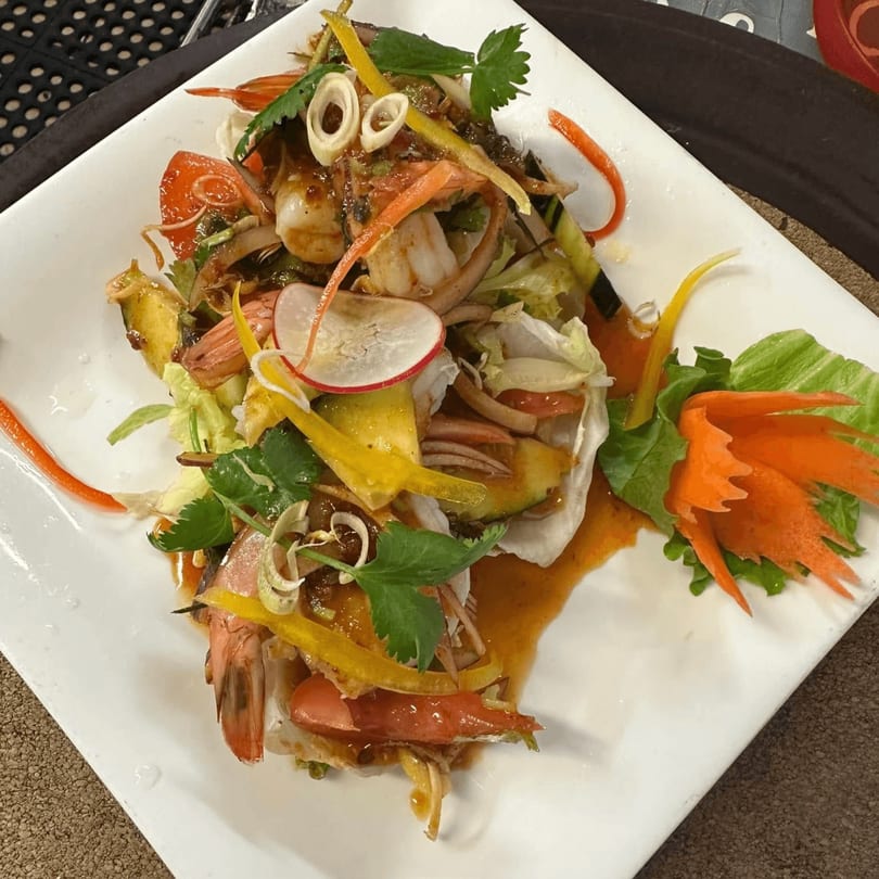 Spicy Thai salad with shrimp, colorful vegetables, and a decorative carrot carving on a white plate.