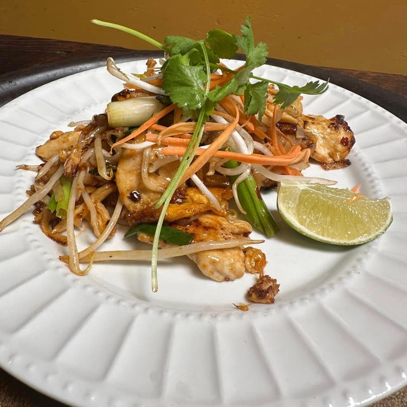 Thai chicken stir-fry with bean sprouts, carrots, onions, cilantro, and a lime wedge on a white plate.