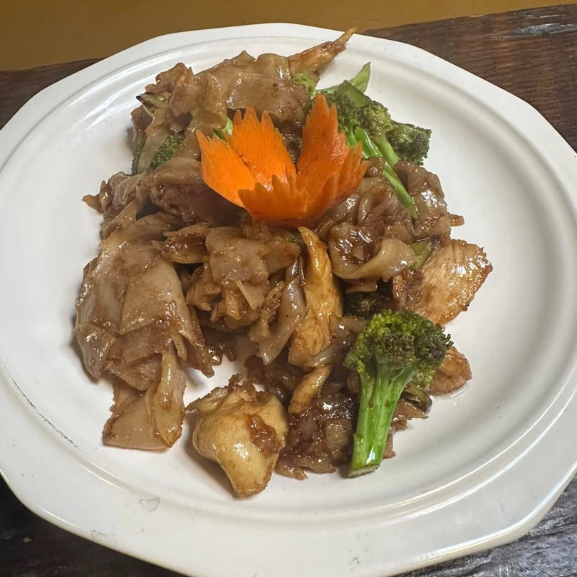 Pad See Ew with chicken, broccoli, and a carved carrot garnish on a white plate.