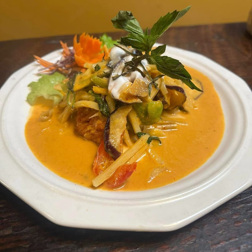Red curry with vegetables, basil, and a dollop of cream on a white plate at Yellow Curry Cozy Thai.