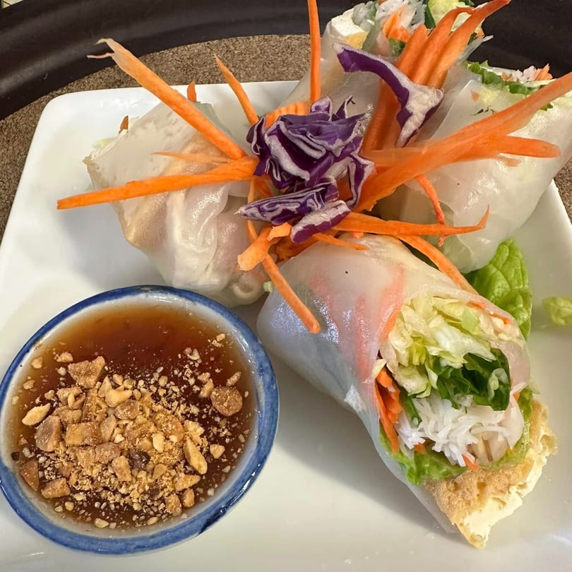 Fresh Thai spring rolls with shredded carrots, cabbage, and lettuce, served with peanut dipping sauce.