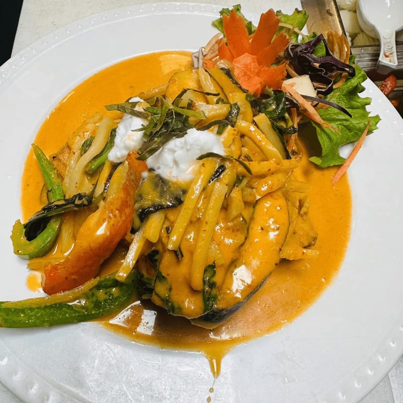 Yellow Curry Cozy Thai dish with vegetables, creamy sauce, and garnish on a white plate.