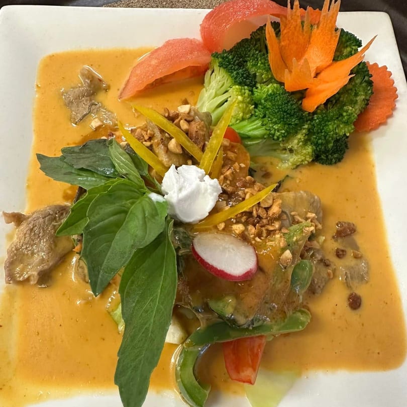 Thai yellow curry with meat, broccoli, basil, and carved carrots on a white plate.