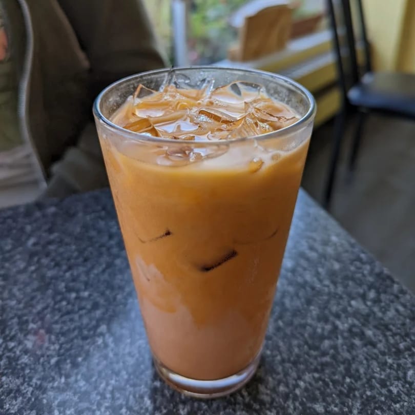 A tall glass of iced Thai tea with a creamy orange hue sits on a dark speckled table.